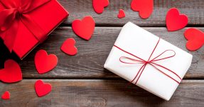Present to a lover on Valentine's Day. Gift boxes near paper hearts on dark wooden background top-down.